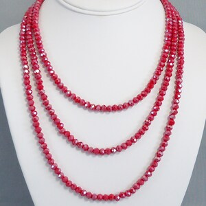 May include: A multi-strand necklace made of red faceted beads. The necklace is layered and has a delicate, feminine look.