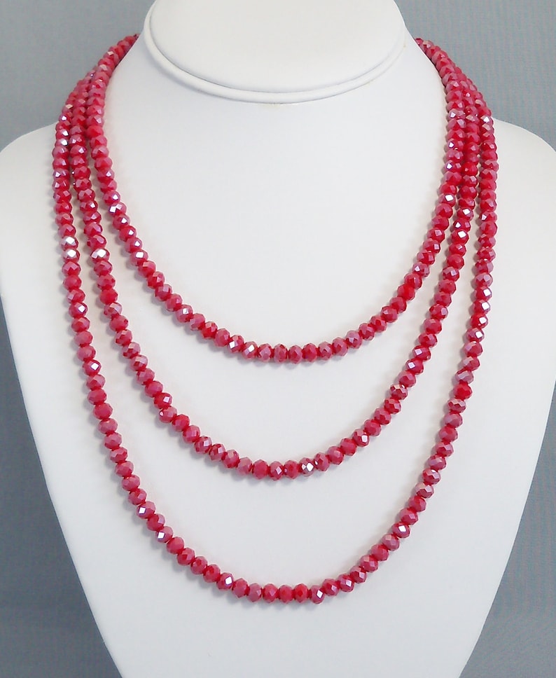 May include: A multi-strand necklace made of red faceted beads. The necklace is layered and has a delicate, feminine look.