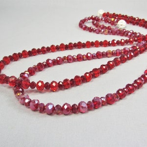 Peut inclure: Un long collier de perles de cristal rouge avec une finition facetée. Les perles sont enfilées sur un fil transparent et sont disposées en plusieurs couches.