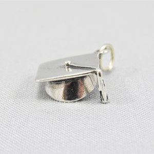 May include: Silver graduation cap charm. The cap is detailed with a tassel and a flat top.