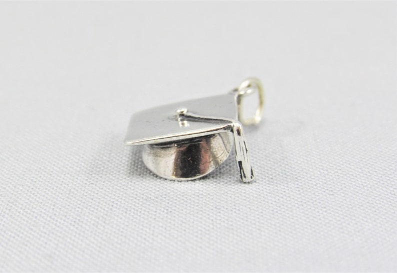 May include: Silver graduation cap charm. The cap is detailed with a tassel and a flat top.