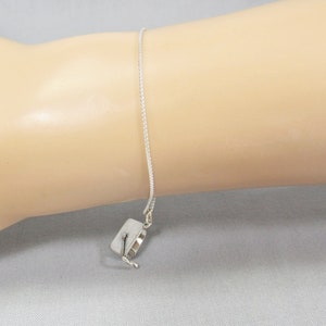 May include: A silver chain bracelet with a small silver charm in the shape of a graduation cap.