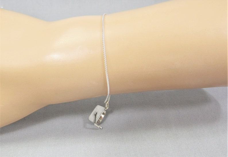 May include: A silver chain bracelet with a small silver charm in the shape of a graduation cap.