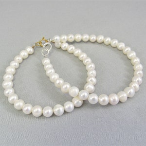 May include: Two white freshwater pearl bead bracelets, one with a sterling spring ring clasp and one with a 14 karat gold fill spring ring clasp.
