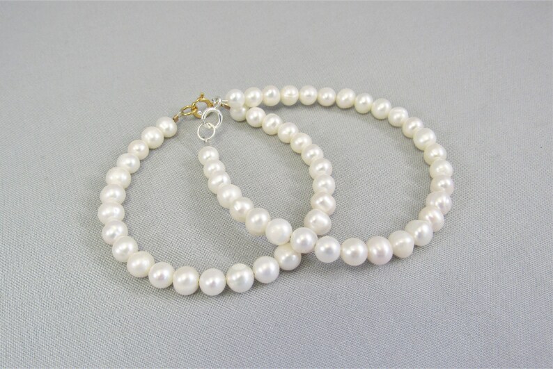 May include: Two white freshwater pearl bead bracelets, one with a sterling spring ring clasp and one with a 14 karat gold fill spring ring clasp.