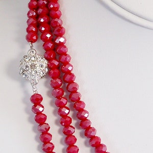 May include: A three-strand necklace made of red faceted glass beads with a silver rhinestone ball clasp.
