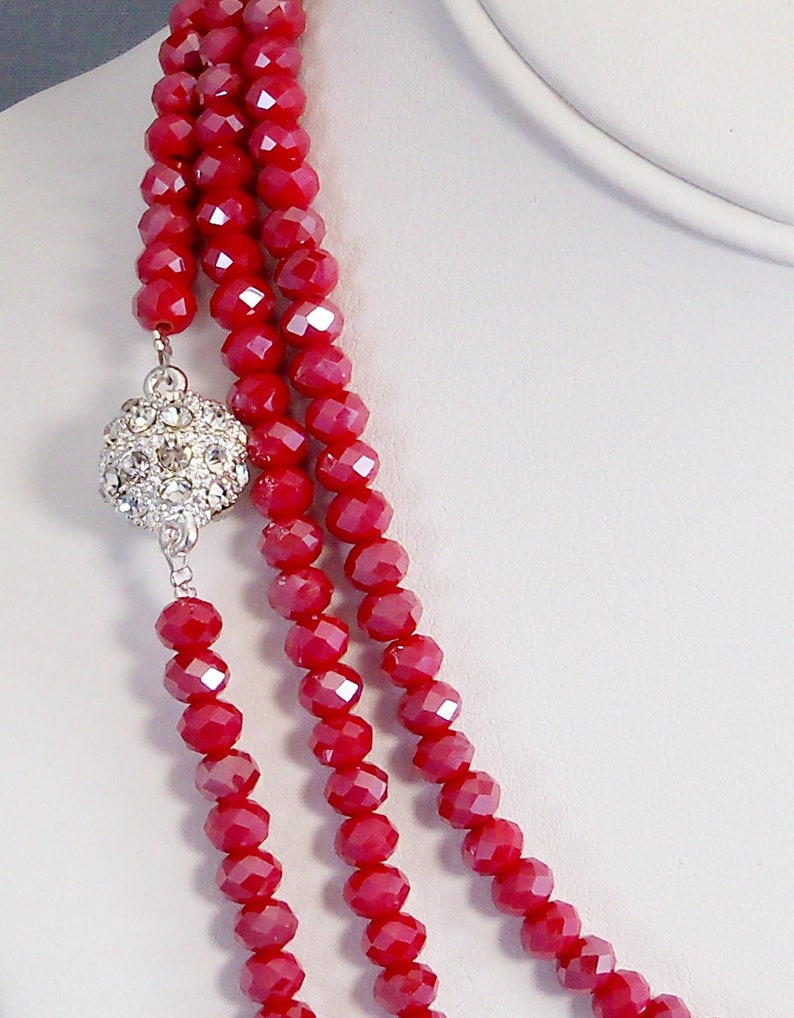 May include: A three-strand necklace made of red faceted glass beads with a silver rhinestone ball clasp.