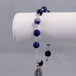 May include: A silver chain bracelet with blue and white gemstone beads and a silver charm of the Virgin Mary.