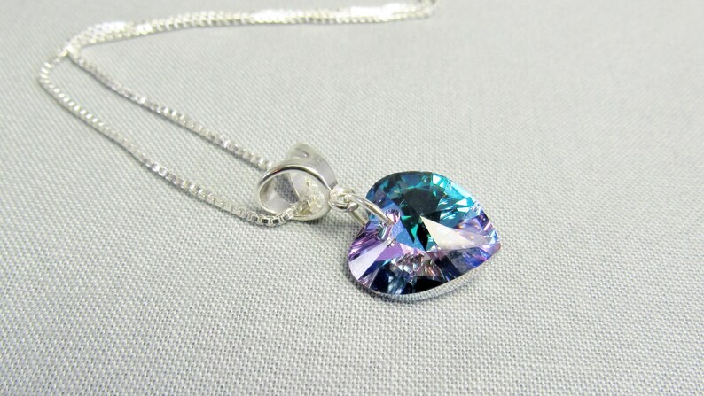 May include: A silver necklace with a heart-shaped pendant. The pendant is a vibrant mix of blue, green, and purple hues. The chain is a delicate silver box chain, and the pendant is attached with a silver bail.