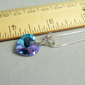 May include: A heart-shaped pendant necklace with a silver chain. The pendant is a gradient of blue and purple. A wooden ruler with inch markings is in the background.