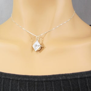 May include: A silver chain necklace with a small silver pendant shaped like a graduation cap. The pendant has a small pearl in the center.