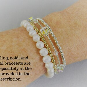 May include: Four bracelets stacked on each other. The top bracelet is silver with small round beads. The second bracelet is gold with small round beads. The third bracelet is silver with small round beads and clear crystal cube beads. The bottom bracelet is white with 6mm round beads. The text on the image reads: 'Sterling, gold, and crystal bracelets are sold separately at the links provided in the description.'