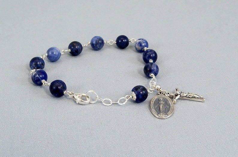 May include: A blue gemstone bracelet with a silver chain and a silver charm featuring the Virgin Mary and a cross.