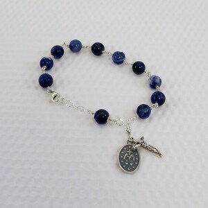 May include: A silver chain bracelet with blue gemstone beads and a silver charm with a cross and a religious symbol.