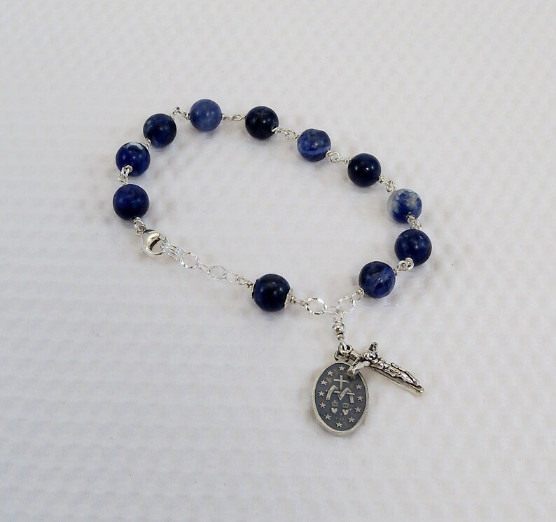 May include: A silver chain bracelet with blue gemstone beads and a silver charm with a cross and a religious symbol.