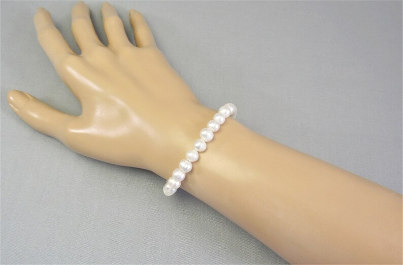 May include: A white pearl bracelet with a simple design. The bracelet is made of round, white pearls that are strung together.