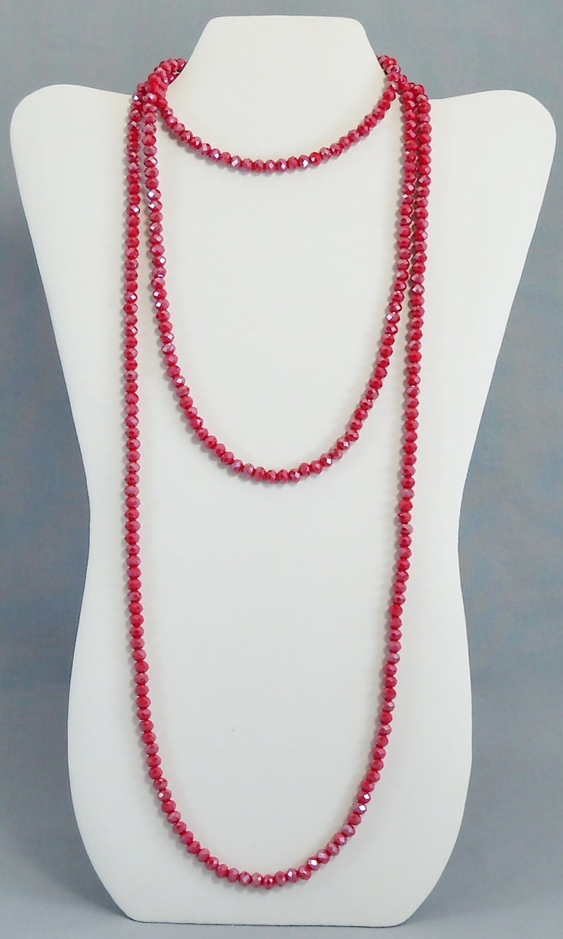 May include: A long, layered necklace made of red faceted beads. The necklace is displayed on a white mannequin bust.