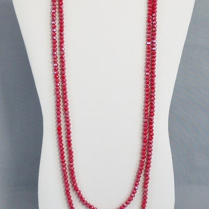 May include: A long, double-strand necklace made of red faceted beads. The necklace is displayed on a white mannequin bust.