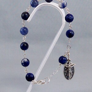 May include: A silver chain bracelet with blue and white gemstone beads and a silver charm with a crucifix.