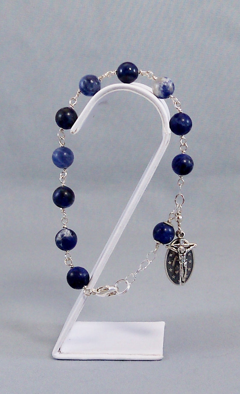 May include: A silver chain bracelet with blue and white gemstone beads and a silver charm with a crucifix.