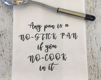 May include: White kitchen towel with black text that reads "Any pan is a NO-STICK PAN if you NO-COOK in it."