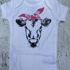 May include: White baby onesie with a black and white cow wearing a pink bandana.