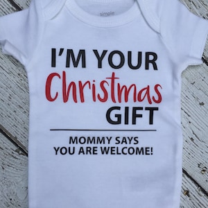 K&ouml;nnte beinhalten: Wei&szlig;er Baby-Strampler mit schwarzem Text, der lautet: "Ich bin dein Weihnachtsgeschenk. Mama sagt, du bist willkommen!"