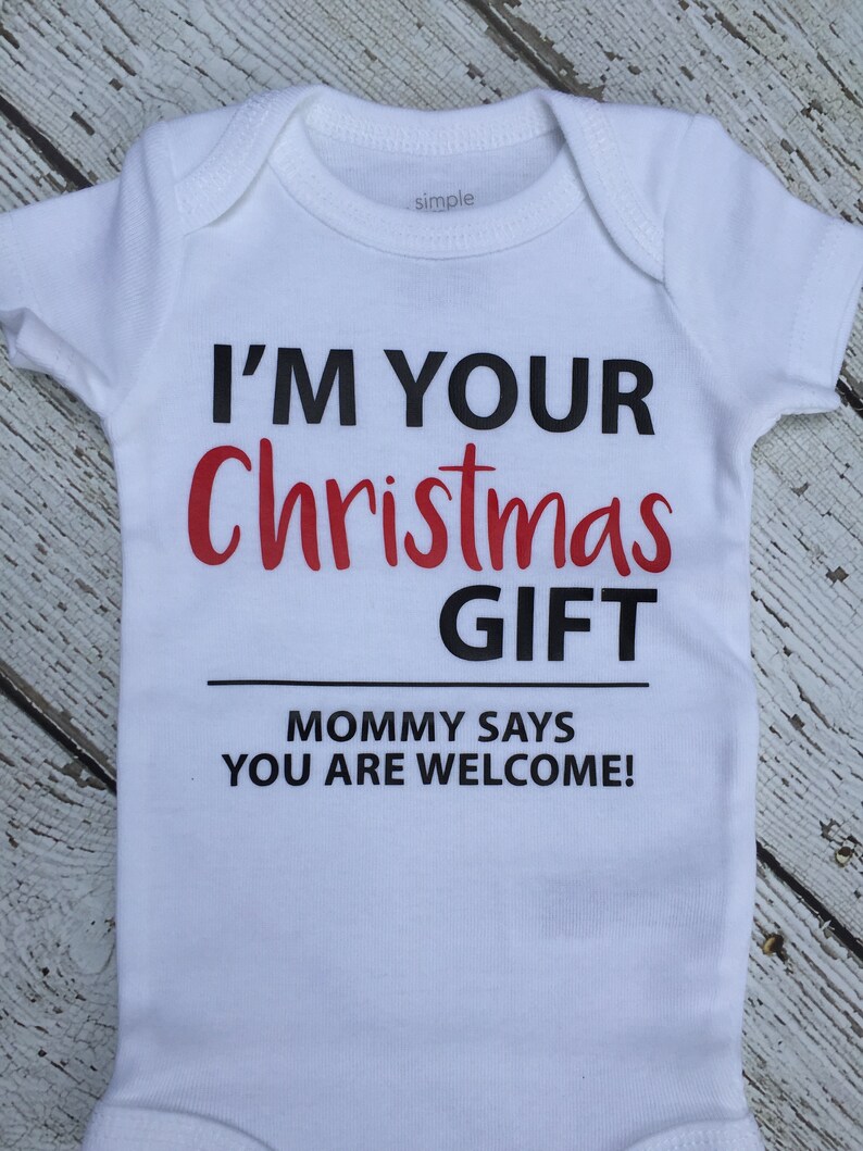 K&ouml;nnte beinhalten: Wei&szlig;er Baby-Strampler mit schwarzem Text, der lautet: "Ich bin dein Weihnachtsgeschenk. Mama sagt, du bist willkommen!"