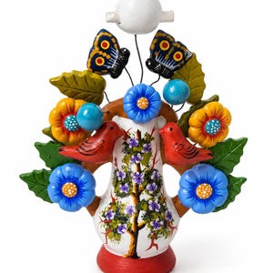 May include: A decorative ceramic tree of life sculpture featuring a white vase base with a painted tree, two red birds, blue and yellow flowers, green leaves, two butterflies, and a white bird perched at the very top of the arrangement.