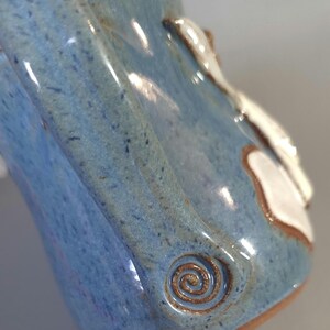 May include: A handmade ceramic mug with a blue glaze and a brown spiral design. The mug has a white accent and a brown rim. The mug is a unique piece of pottery.