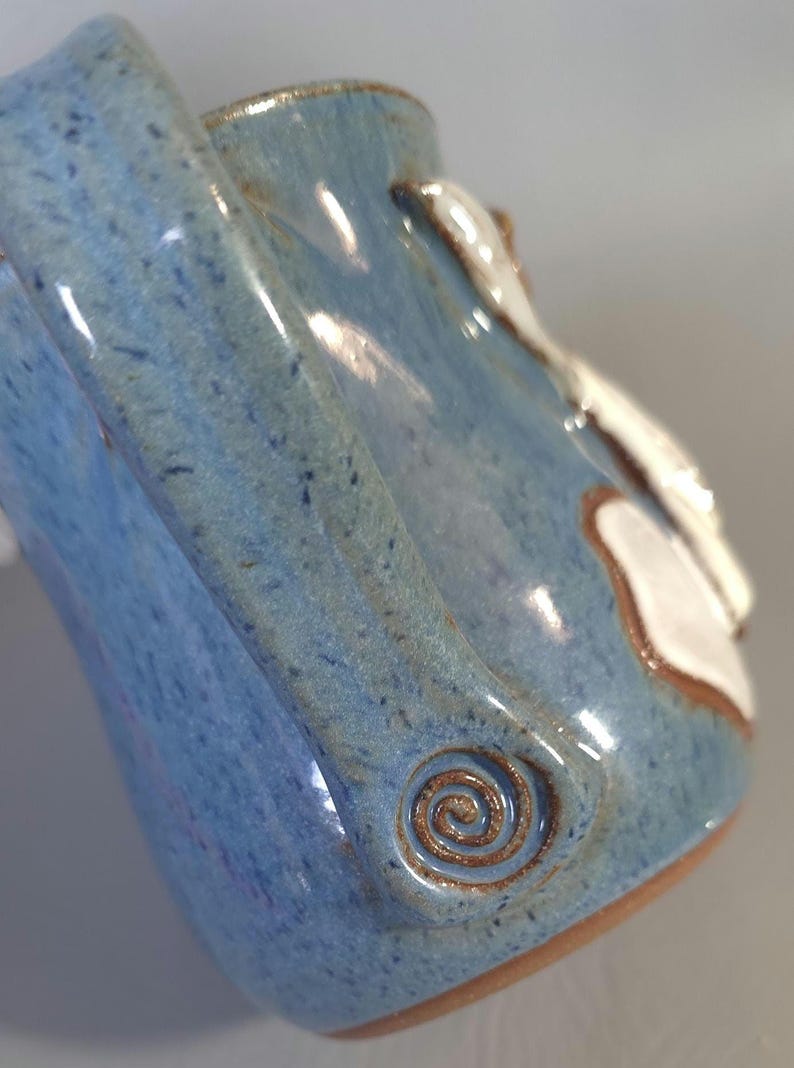 May include: A handmade ceramic mug with a blue glaze and a brown spiral design. The mug has a white accent and a brown rim. The mug is a unique piece of pottery.