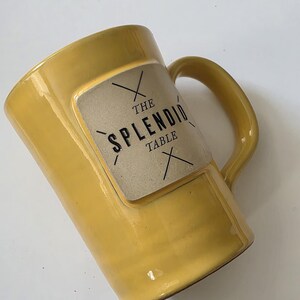May include: A set of three ceramic mugs with a speckled, matte finish. The mugs are in shades of cream, light gray, and dark gray. Each mug has a simple, minimalist design and a rounded handle. The mugs are likely for coffee or tea.