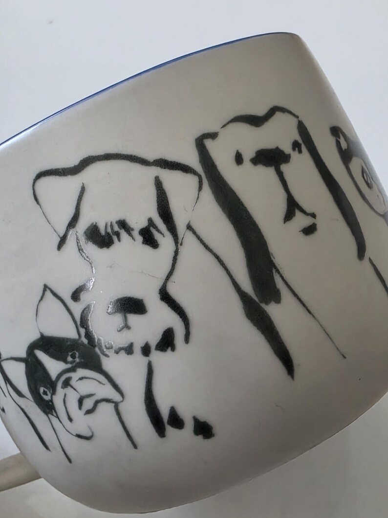 May include: White ceramic mug with a blue rim, featuring black line drawings of various dog breeds. The mug's design includes several dog illustrations, showcasing different shapes and sizes.