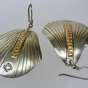 May include: A pair of silver earrings with a gold accent. The earrings are shaped like a fan and have a textured surface.