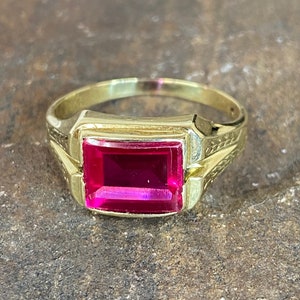 May include: A gold ring with a large, rectangular, bright red gemstone.