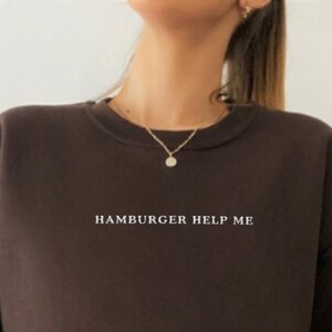 May include: A brown sweatshirt with the text "HAMBURGER HELP ME" printed in white on the front.