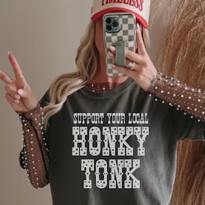 May include: A gray t-shirt with the text 'Support Your Local Honky Tonk' in white with stars around the letters.