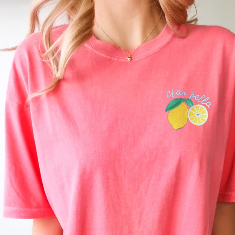 May include: A pink t-shirt with a lemon graphic and the text "Ciao Bella" embroidered on the front.