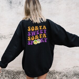 May include: Black sweatshirt with the text "Sorta Sweet Sorta Spooky" in orange, purple, and green. The design includes a pumpkin, ghost, and bat graphic, perfect for Halloween.