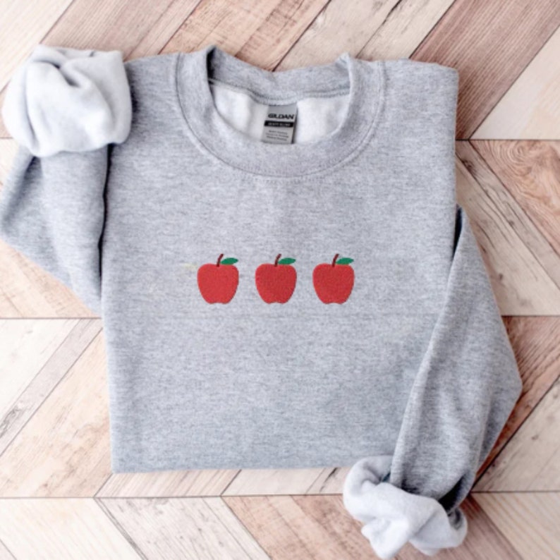 May include: A gray sweatshirt with three red apples embroidered on the front. The apples have green stems and leaves.