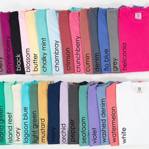 May include: A collection of 28 folded t-shirts in various colors, including bay, berry, boysenberry, black, blossom, butter, chalky mint, chambray, crimson, crunchberry, cumin, denim, flo blue, grey, heliconia, ice blue, island green, island reef, ivory, lagoon blue, light green, mustard, navy, orchid, pepper, seafoam, violet, washed denim, watermelon, and white.