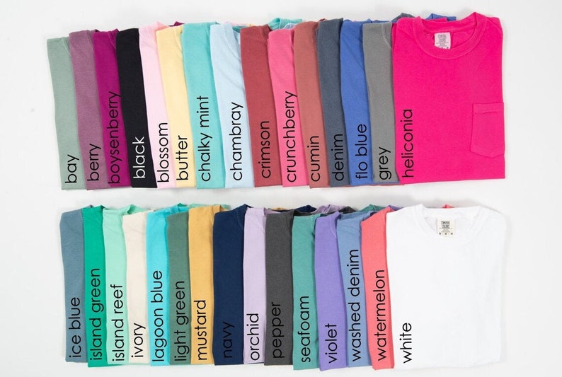 May include: A collection of 28 folded t-shirts in various colors, including bay, berry, boysenberry, black, blossom, butter, chalky mint, chambray, crimson, crunchberry, cumin, denim, flo blue, grey, heliconia, ice blue, island green, island reef, ivory, lagoon blue, light green, mustard, navy, orchid, pepper, seafoam, violet, washed denim, watermelon, and white.