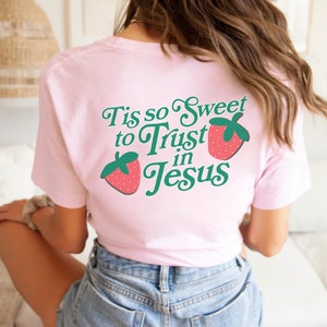 May include: Pink t-shirt with a green and red graphic that says "Tis so Sweet to Trust in Jesus" with two strawberries on either side of the text.