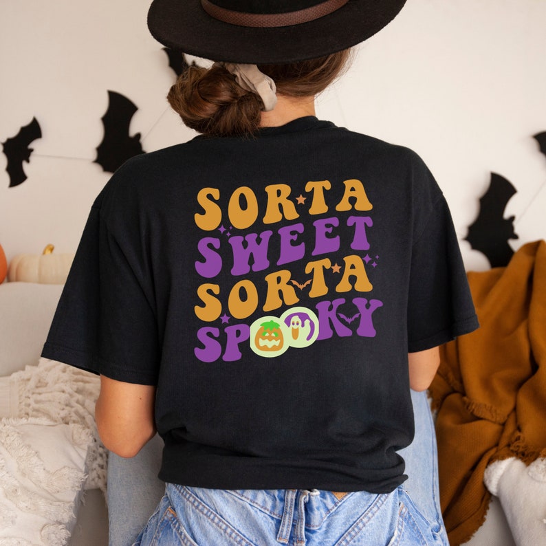 Pode incluir: Camiseta preta com um gr&aacute;fico de estilo retro que diz "Sorta Sweet Sorta Spooky" com uma ilustra&ccedil;&atilde;o de ab&oacute;bora e fantasma.
