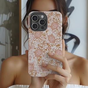May include: A white phone case with a pink and brown pattern of stylized turtles and flowers. The case has a black camera bump with four lenses.