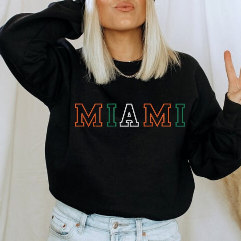May include: Black sweatshirt with the word "MIAMI" printed in white, green, and orange letters with a white outline.