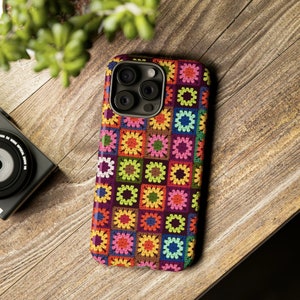 May include: A colourful phone case with a crocheted granny square pattern in shades of pink, green, yellow, blue, and brown. The case has a cutout for the phone's camera.