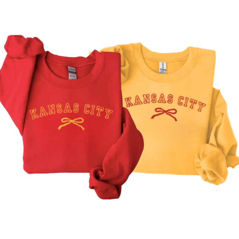 May include: Two sweatshirts with the text "Kansas City" in red with a yellow bow. One sweatshirt is red and the other is yellow.