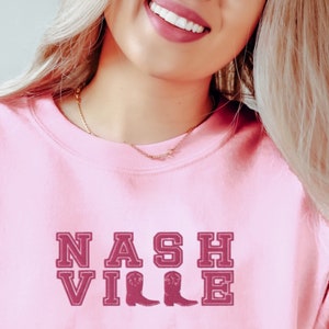 May include: Pink sweatshirt with a maroon graphic that says "NASHVILLE" with two maroon cowboy boots.