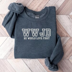 May include: A dark gray sweatshirt with the text "WWJD HE WOULD LOVE FIRST" in white.